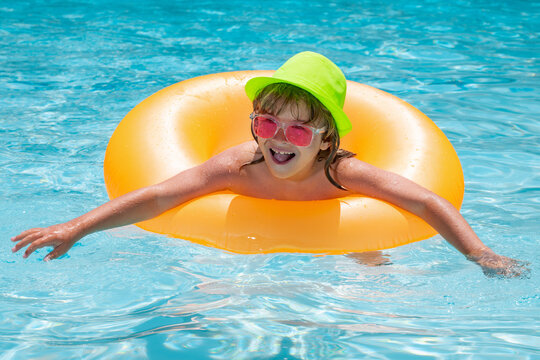 Child swin in swimming pool on inflatable ring. Kid swim with orange float. Water toy, healthy outdoor sport activity for children. Fashion summer kids in hat sunglasses.