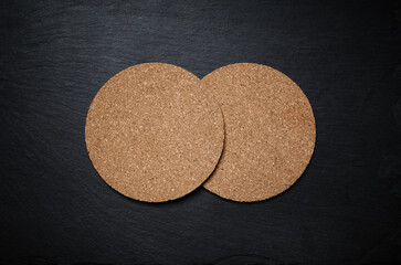 Photo of two blank cork beer coasters on black stone slate plate. Copy space for text. Flat lay.