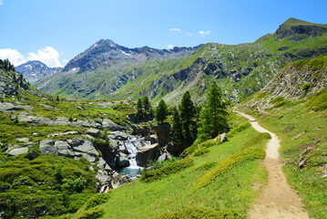 Fototapeta na wymiar Gran Paradiso National Park. Hiking trail in the Valle di Bardoney, Aosta Valley, Italy. Beautiful mountain landscape in sunny day.