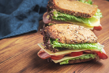 Sandwich with a ham, cheese, tomato, salad lettuce on a wooden board