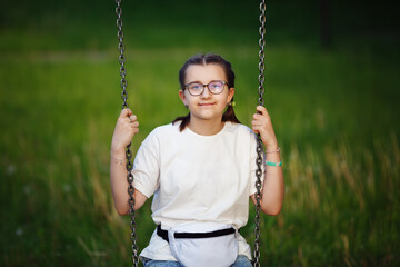 Close-up of a teen girl in glasses posing sitting on a swing.