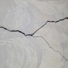 Large uneven cracks on a gray plastered surface. A cracked concrete wall covered with cement...