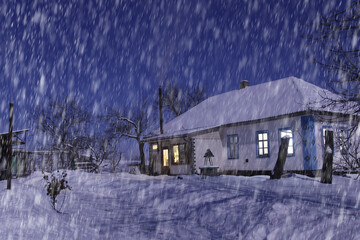 Beautiful view of the snow-covered house at night during heavy snowfall. Everything is covered in snow. Smoke comes from the chimney.