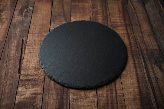 Photo of round slate plate on wooden background. Copy space.
