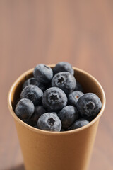 Fresh organic blueberries in papaer cup on wood table with copy space