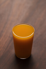 orange, pumpkin and carrot mixed juice in tumbler glass on walnut table