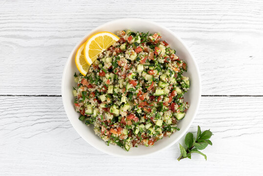 Tabbouleh salad with quinoa, tomatoes, cucumbers, parsley, mint and lemon juice on a white background. Top view. Healthy vegetarian salad. 