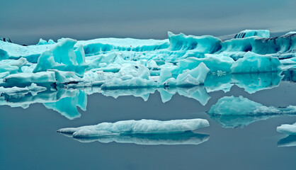 Reflections of crystal blue and white ice floes in black dark glassy smooth water in dim gloomy...