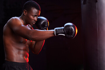 Boxer, fitness and black man isolated on a dark background or gym training focus, challenge and bodybuilder fist impact. Strong, power and boxing athlete or sports person with exercise in mma gear - Powered by Adobe