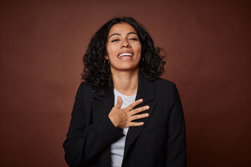 A young business colombian woman laughs out loudly keeping hand on chest.