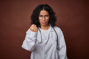 Young colombian doctor woman with stethoscope showing fist to camera, aggressive facial expression.