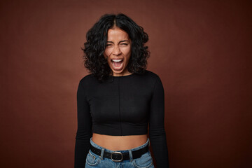 Young colombian curly hair woman isolated on brown background shouting very angry, rage concept,...