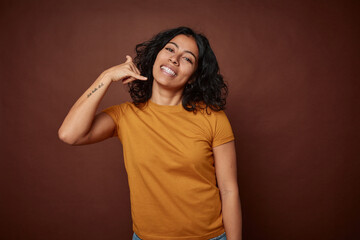 Young colombian curly hair woman isolated on brown background showing a mobile phone call gesture with fingers.