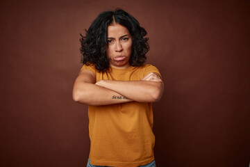 Young colombian curly hair woman isolated on brown background shrugs shoulders and open eyes...