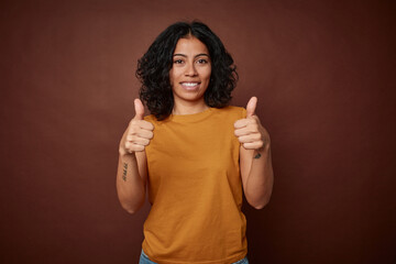 Young colombian curly hair woman isolated on brown background smiling and raising thumb up