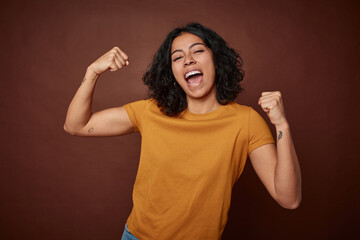 Young colombian curly hair woman isolated on brown background raising fist after a victory, winner...