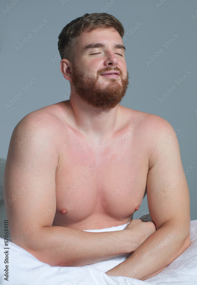 Poster Young happy handsome sleepy man in the bed in bedroom at home in the morning lying under white blanket, enjoy resting, sleep well in night mask on face, eyes. Vertical photo 