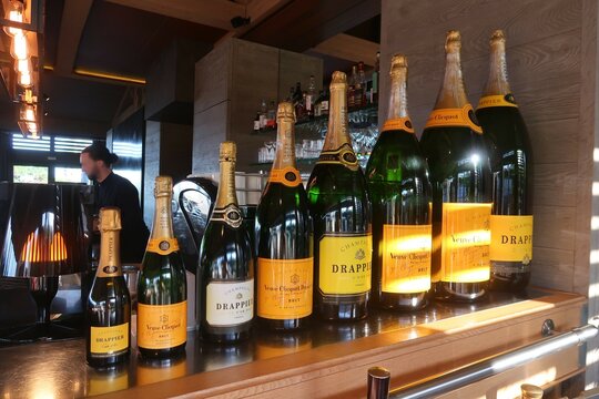Huit bouteilles de champagne des marques Veuve Cliquot et Drappier sur le comptoir d&rsquo;un bar restaurant, class&eacute;es par taille, de la plus petite contenance &agrave; la plus grande - novembre 2022 (France)