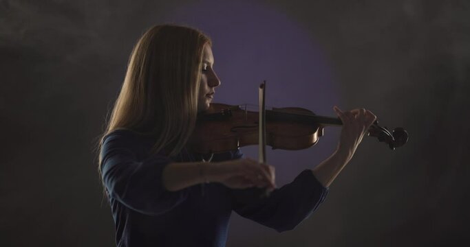 Beautiful blond woman playing violin against blue and violet smoke background.