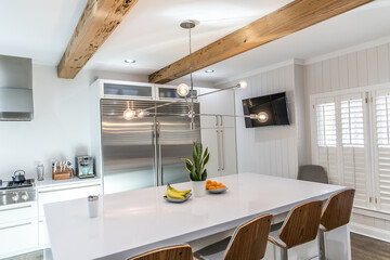 A large luxury modern kitchen with white walls and wood beams and a large quartz quartzite island