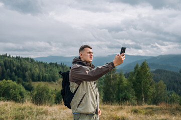 A male tourist with a smartphone in his hands is looking for a mobile network in the mountains with...