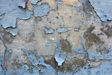 The gray flat concrete wall painted long ago with blue, light blue paint has already cracked, deep cracks on the wall are visible and it has peeled off in a long time.