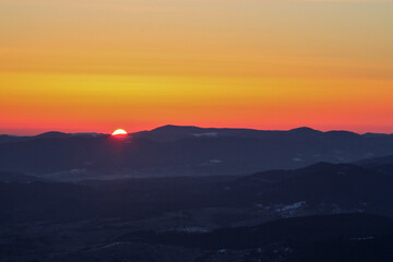 Orange sky at sunrise in dark winter mountains