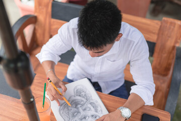 A talented visual artist uses a pencil and a blank sketchpad as a medium to create an artwork.