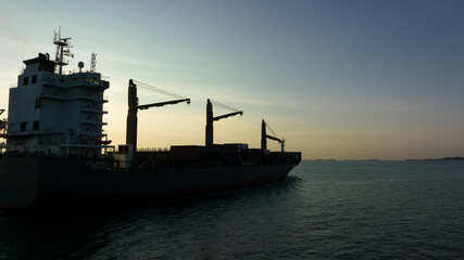 Obraz premium corgo ship container in silhouette and over the sunlight at evening in open sea. aerial view