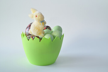 Wielkanocny zając siedzący na pisankach umieszczonych w zielonym naczyniu w kształcie skorupki jajka na jasnym tle.