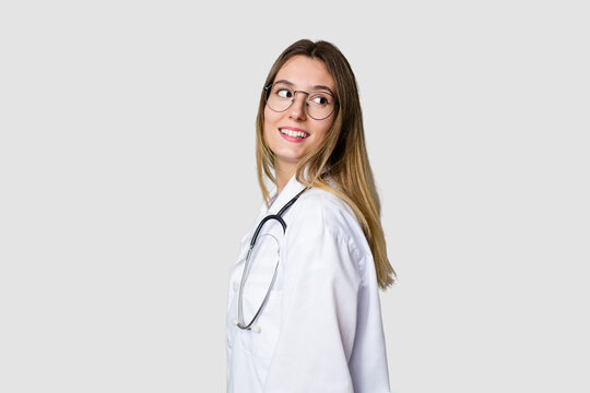 Compassionate female physician with a stethoscope around her neck, ready to diagnose and care for her patients in her signature white coat looks aside smiling, cheerful and pleasant.