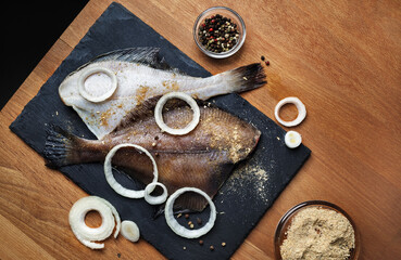 Plaice with spices, pepper and onions onslate cutting board. Flounder prepared for cooking. Flat lay.