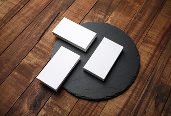 Blank business cards and round slate plate on wooden background.