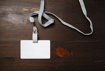 Photo of blank plastic id badge with lanyard on wood table background. Copy space for text. Flat lay.