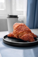 Coffee and croissant for breakfast. Paper cup for coffee. A mockup of the beverage cup. Laptop on the dining table. Work at breakfast. Coffee break. Croissants on a plate and a cup of tea. Pastries.
