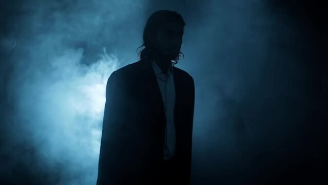Shot of a young assassin with long hair. A young hitman with long hair coming from the darkness and shooting bullets, Cinematic light, and some smoke. HD footage 24 FPS.