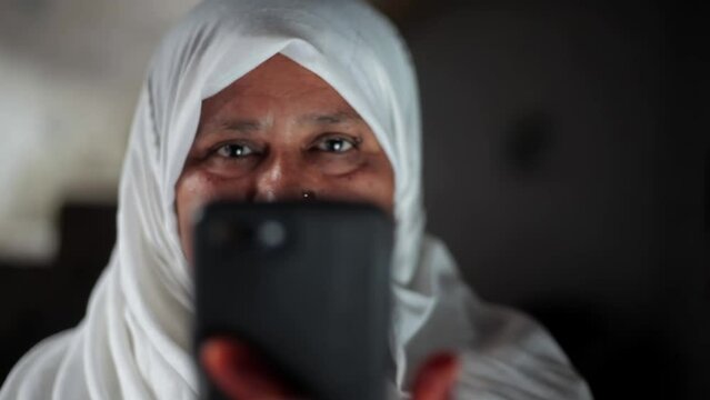 Muslim woman in white colored hijab using a black colored phone and smiling. Muslim woman using technology.