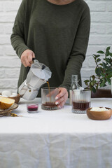 a woman is pouring coffee in glass on light table for breakfast.