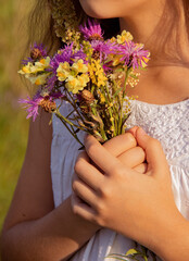Obraz na płótnie Canvas Teen girl wearing white dress holding wild flowers bouquet on a grassy sunny summer meadow field