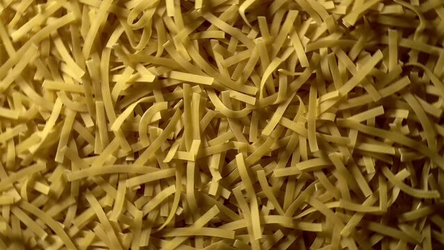 Uncooked Tagliatelle Lungo pasta rotating in fast motion - top view, flat lay, low key, food background. Raw dried organic golden long macaroni texture. Italian food, cuisine and culture close up