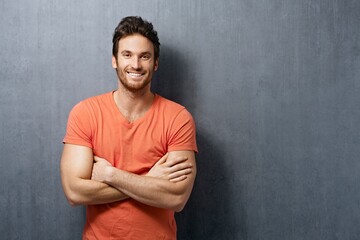 Portrait of happy white young man smiling, standing against white concrete wall. Copy space, casual clothing.
