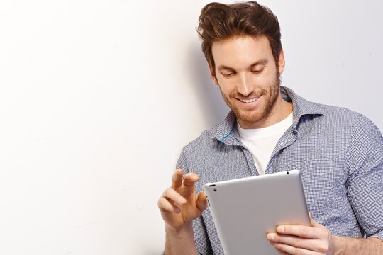Happy white man working using tablet computer leaning against white wall. Copy space, casual clothing.