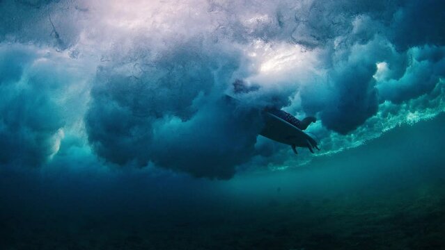 Surfer underwater. Man dives under the wave with surfboard to pass the wave. Underwater view of the surfer duck diving under the wave