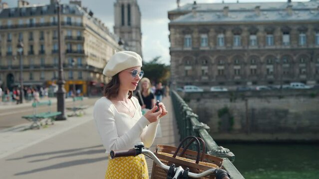 Attractive girl with bicycle painting her lips on a bridge in Paris