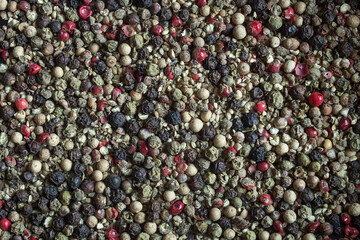Top-down view of mixed peppercorns in black, white, and green showing diversity in color and texture. Ideal for promoting healthy cooking and adding flavor to dishes. Organic texture background.