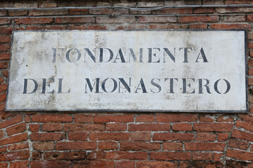 Fototapeta na wymiar Venetian street sign on the monastery brick wall. View of the Fondamenta del Monastero in Venice, Italy
