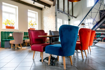 A modern cozy restaurant with colorful upholstered chairs and comfortable sofas. Unusual cafe design with rough concrete walls and wooden decorative beams on the ceiling.