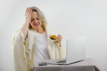 headache woman holds hand onr head and twisted mouth hands tea with lemon on table laptop phone white background pricks on back cold one disease cold coronavirus convalescence prescription drugs drugs