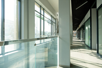 A corridor in an urban-type office building. Modern interior of the lobby of an office building with glass doors, walls and large spacious windows. A lighted long corridor in a modern business center