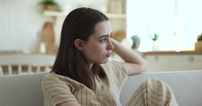 Lost in sad thoughts girl sit on couch, thinks, staring into distance feels emptiness by personal concerns, looks lonely and frustrated, having bored weekend alone at home. Low self-esteem, problems